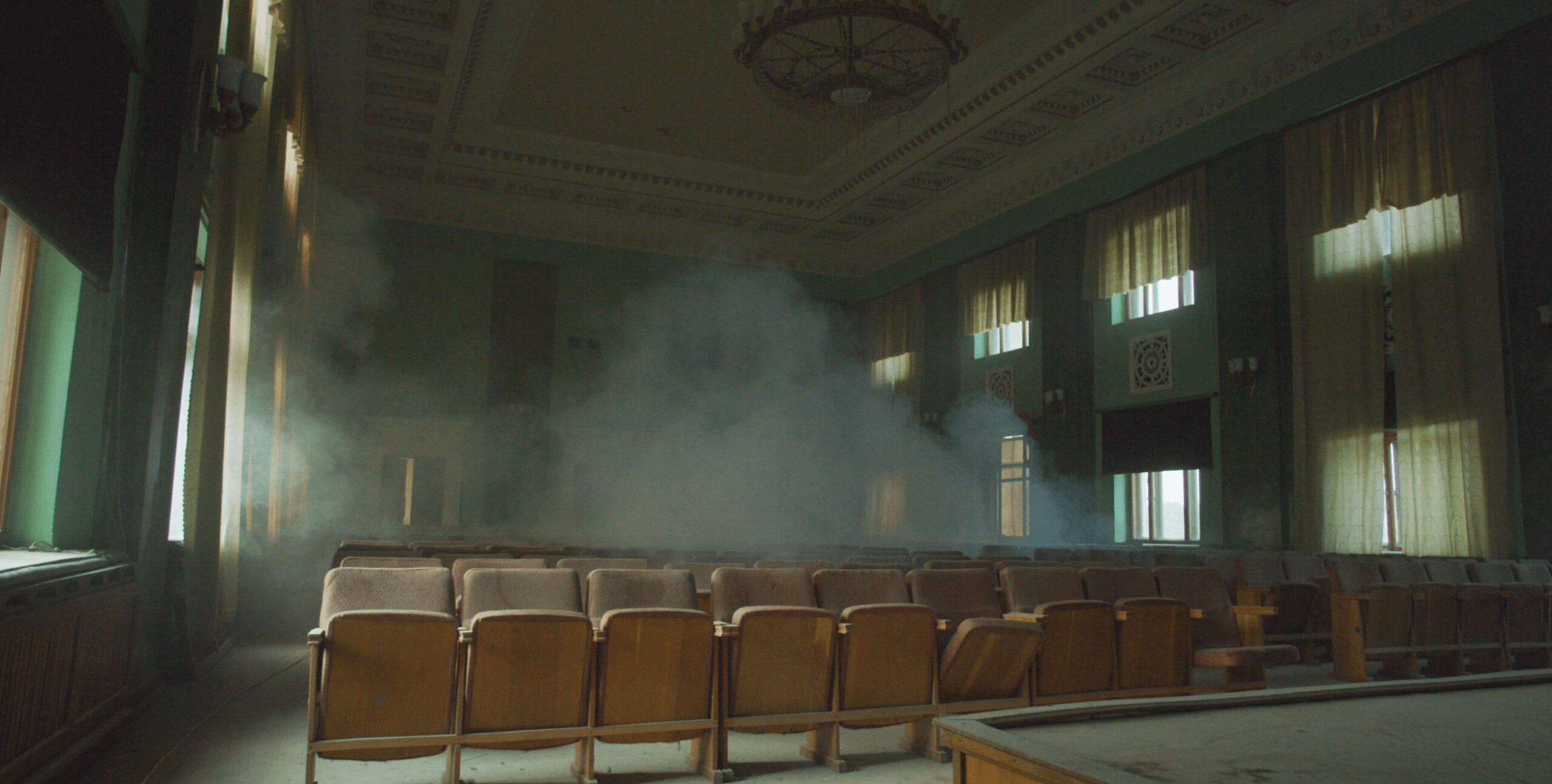 video still, view from the stage of an empty auditorium filled with smoke or dust