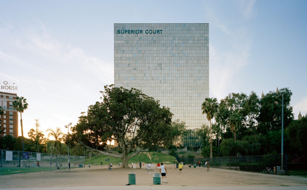 Photograph of people playing soccer on a dirt patch in Lafayette Park. In the background looms the Superior Court building.